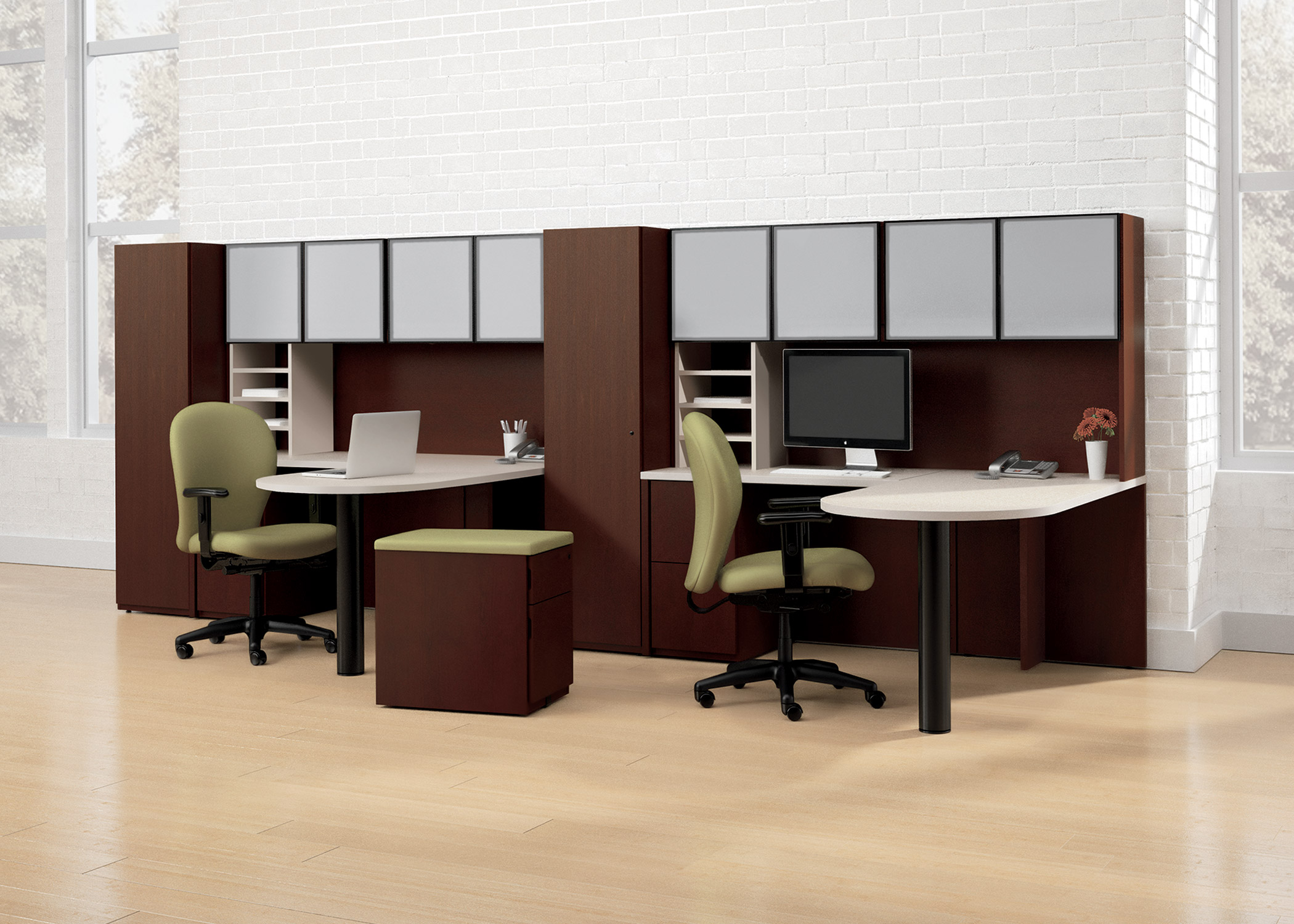 Two toned shared office space designed with Nationa's Renegade products. Both desk set ups include a white laminate work surface with all other casegoods in a mahogany finish. Desk units include frosted glass overhead bins, a storage cabinet, and an undersurface pedestal. Peninsula on these units is supported by a black column leg. Task chairs are black framed with a sage colored fabric. One random pedestal is in the middle of the room with mahogany colored laminate and a sage green fabric top.
