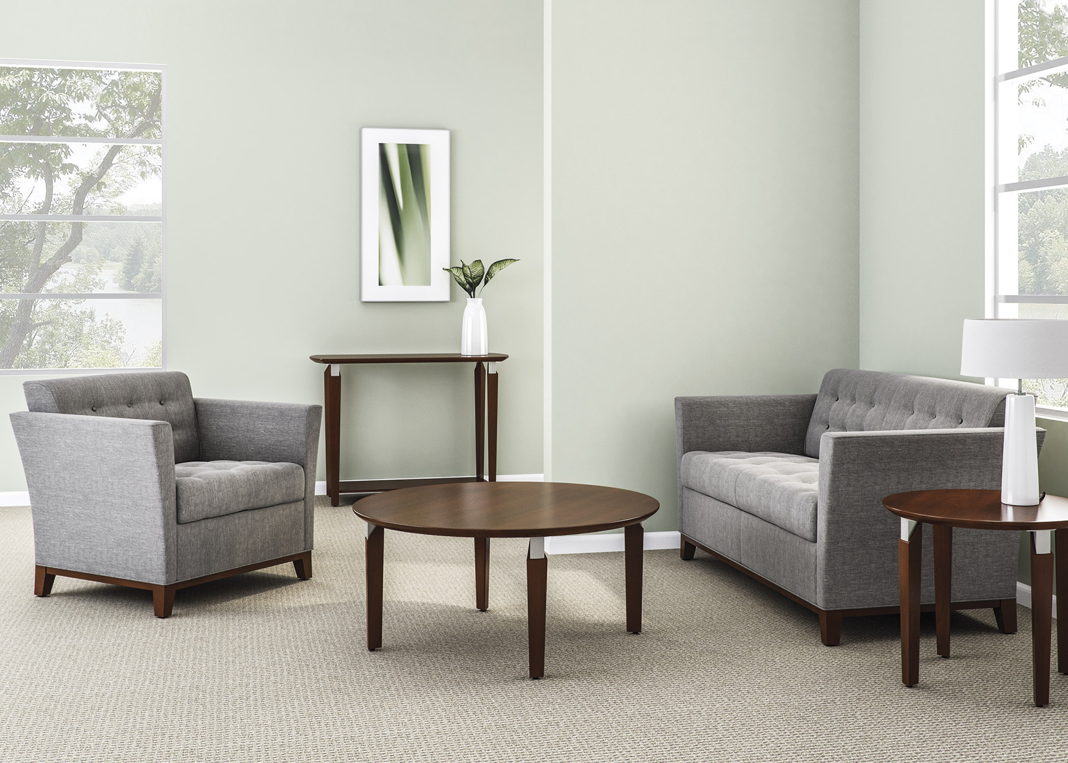 Room designed with National brand Monterrey lounge furniture in a grey and white fabric. There is a love seat and single chair across from each other in the room. A mahogany colored console table is against the back wall, while the mahogany coffee table is centered in the room, and the mahogany end table is next to the love seat. Room is accessorized with white decor and wall art.