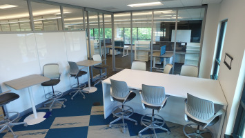 White desks and chairs with a wall whiteboard for written collaboration and brainstorming.