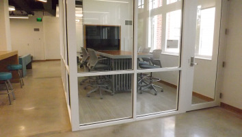 Glass privacy wall enclosing a media:scape table and tv monitor with four chairs surrounding the table