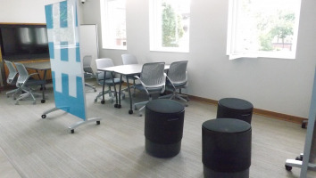 Three black Steelcase Buoy seats with a Clarus freestanding glassboard and two sets of fliptop tables and Steelcase Cobi chairs with platinum frames and grey seats.