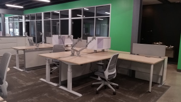 Office with several height adjustable desks and mesh back chairs.