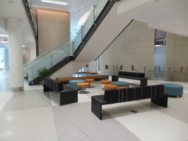 Brown benching in a lobby area underneath a staircase with blue and orange seating that serves as ottomans.