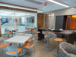 Orange Coalesse Enea stools in cafeteria area with three tables, deep mahogany counter top and multicolored lounge seating.