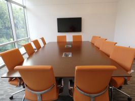 Conference room with long table equipped with digital inputs/outputs, cherry laminate conference table with twelve orange conference chairs and a multimedia television for conferencing.