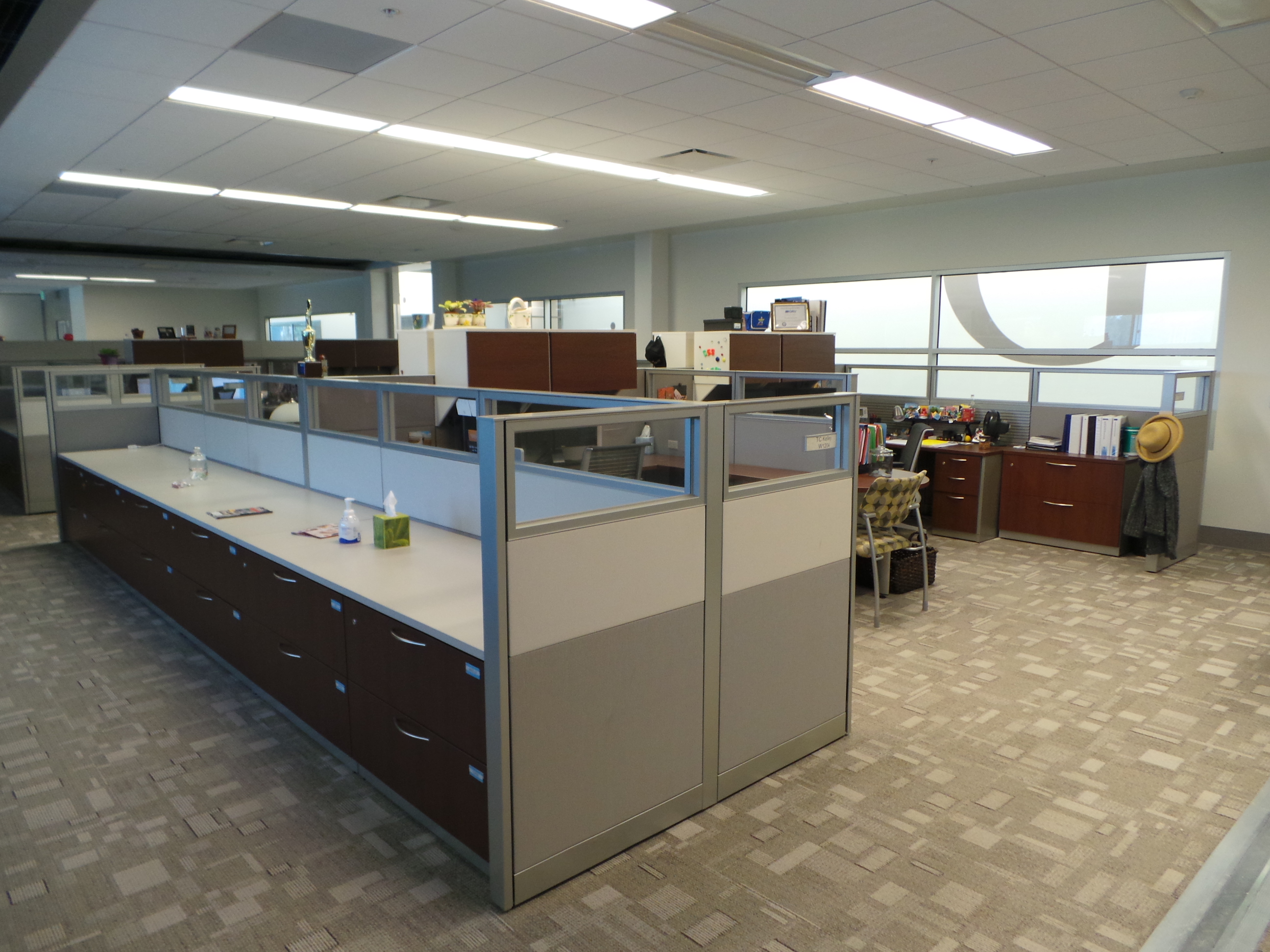 Workstations created with panel systems and storage cabinets with a laminate top for open use. Separate offices behind workstations with cherry laminate desking and multicolored guest chairs.