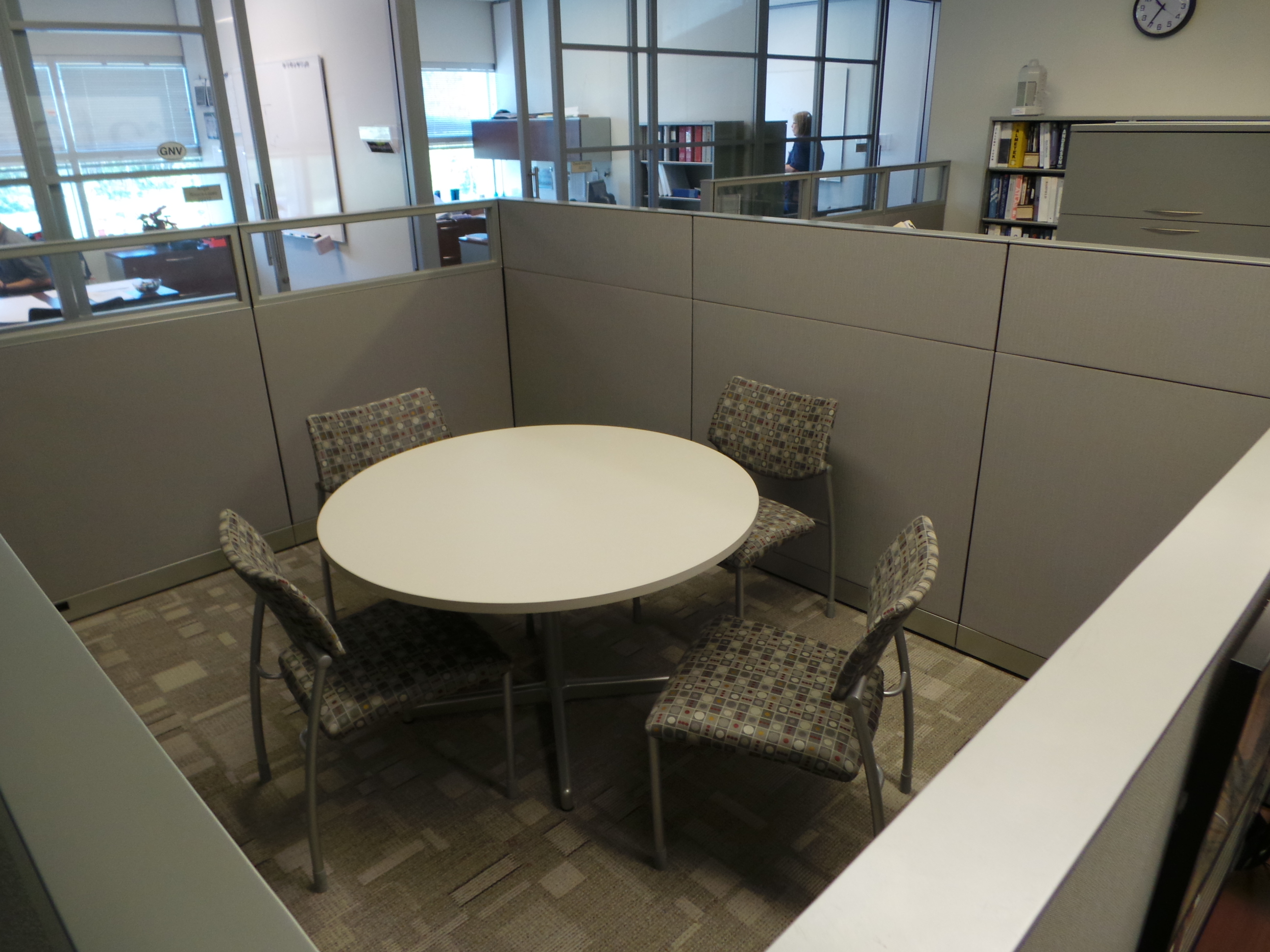 Private meeting space with a white table and four multicolored guest chairs inside of a cubicle separated space.