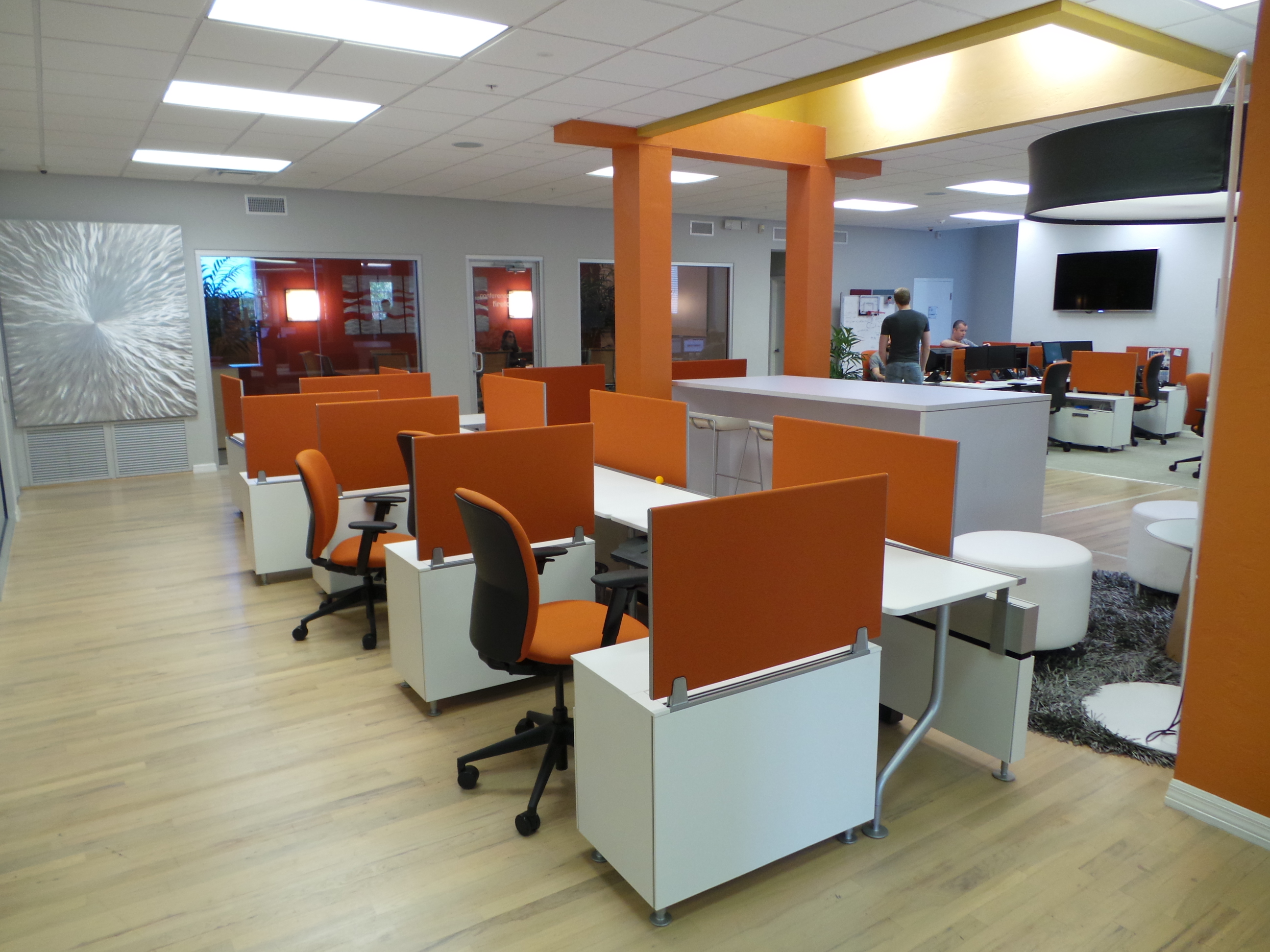 Hotel desking with orange chairs and orange privacy screens with white ottomans in a central lobby location