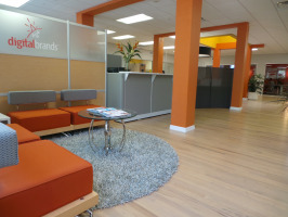 Four red single sofas in a lobby area with orange colored wall posts, a grey reception area and a grey rug.