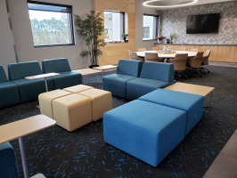 Various shades of blue lobby seaing with beige ottomans and blonde laminate end tables. White round conference table in background with eight beige conference chairs.