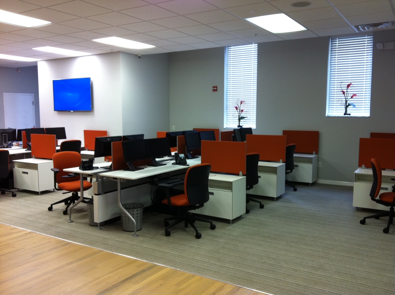 Hotel desking with white storage bins, red chairs and black monitors.