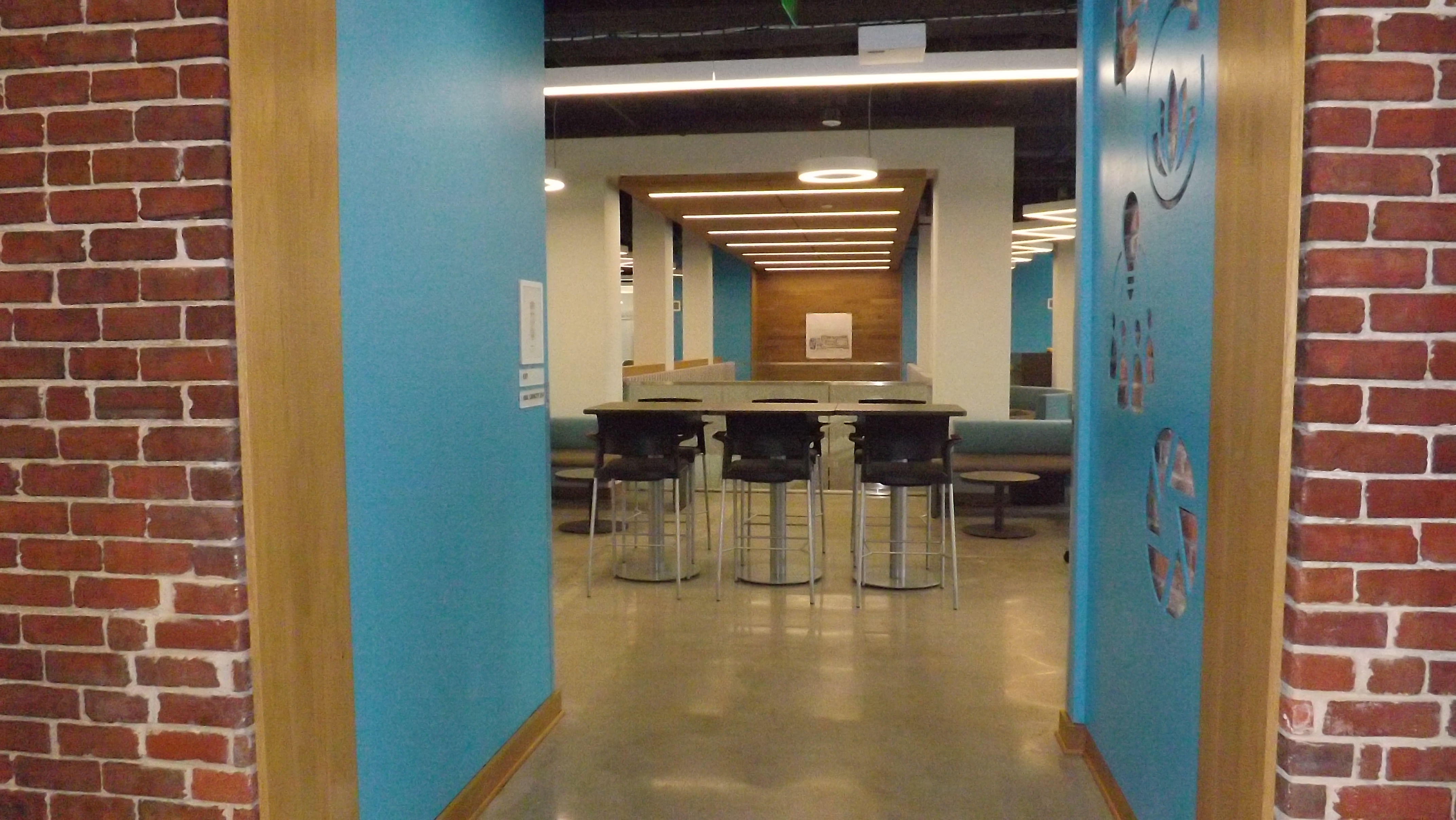 Red brick entryway with blue embellishments leading to a lobby area with cafe seating and tables.