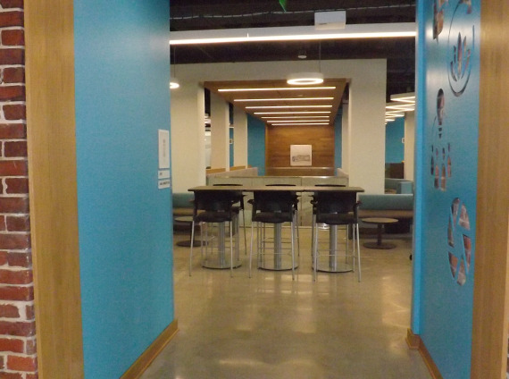 Red brick entryway with blue embellishments leading to a lobby area with cafe seating and tables.