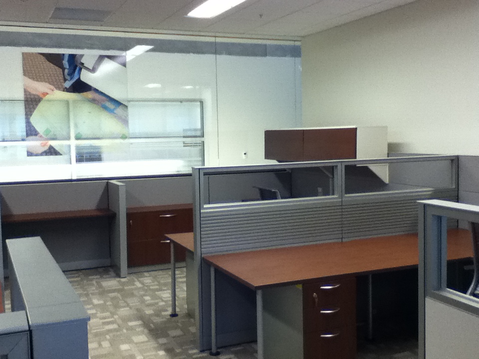 Cubicle desking with glass stackers on top of pabels, with cherry laminate desking and filing cabinet under desk.